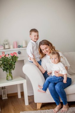 Güzel genç anne, küçük oğlu, küçük kızı evde kanepede oturuyor. Anneler Günü. Mutlu bir aile. Rahat.