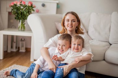 Güzel genç anne, küçük oğlu, küçük kızı evde kanepede oturuyor. Anneler Günü. Mutlu bir aile. Rahat.