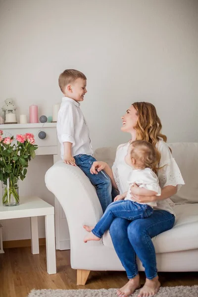 Bela mãe, filhinho, filhinha estão sentados no sofá em casa. Dia das Mães. Uma família feliz. Aconchegante . — Fotografia de Stock