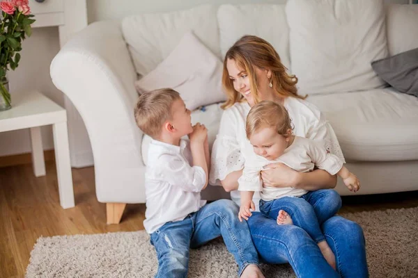 Beautiful young mother, little son, little daughter are sitting on the sofa at home. Mothers Day. A happy family. Cozy. — Stock Photo, Image