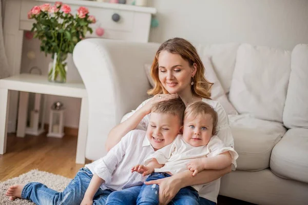 Mooie jonge moeder, kleine zoon, kleine dochter zitten op de Bank thuis. Moederdag. Een gelukkige familie. Gezellige. — Stockfoto