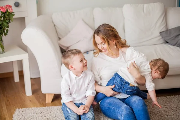 Mooie jonge moeder, kleine zoon, kleine dochter zitten op de Bank thuis. Moederdag. Een gelukkige familie. Gezellige. — Stockfoto