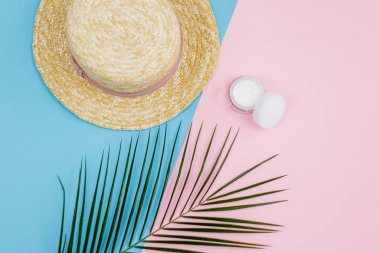 Tropical plant, female straw hat, cream in a jar on a blue with a pink background.