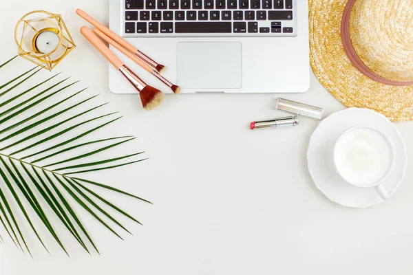 Pianta tropicale, cappello di paglia da donna, computer portatile, tazza di cappuccino, cosmetici, spazzole, candela su sfondo bianco. Cose da donne . — Foto Stock