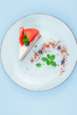 A beautiful piece of cake with berries with butter cream on a blue background. Cake with red cakes.