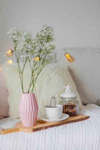 Spring home cozy interior. A bouquet of flowers in a vase, a cup of tea, decor on the sofa. Mood.