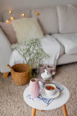 Evin içi bahar havası. Vazoda bir buket çiçek, bir fincan çay, sehpanın üstünde dekor. Ruh hali.