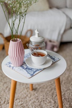 Evin içi bahar havası. Vazoda bir buket çiçek, bir fincan çay, sehpanın üstünde dekor. Ruh hali.