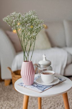 Evin içi bahar havası. Vazoda bir buket çiçek, bir fincan çay, sehpanın üstünde dekor. Ruh hali.