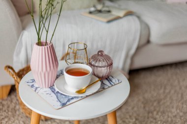 Evin içi bahar havası. Vazoda bir buket çiçek, bir fincan çay, sehpanın üstünde dekor. Ruh hali.