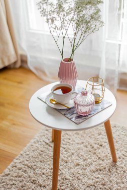 Evin içi bahar havası. Vazoda bir buket çiçek, bir fincan çay, sehpanın üstünde dekor. Ruh hali.