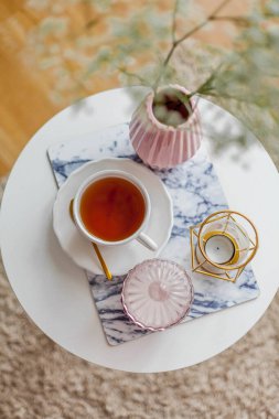 Evin içi bahar havası. Vazoda bir buket çiçek, bir fincan çay, sehpanın üstünde dekor. Ruh hali.