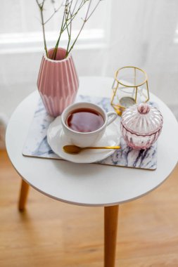 Evin içi bahar havası. Vazoda bir buket çiçek, bir fincan çay, sehpanın üstünde dekor. Ruh hali.