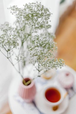 Evin içi bahar havası. Vazoda bir buket çiçek, bir fincan çay, sehpanın üstünde dekor. Ruh hali.