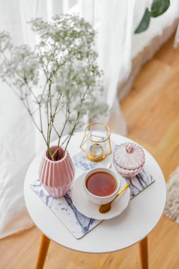 Evin içi bahar havası. Vazoda bir buket çiçek, bir fincan çay, sehpanın üstünde dekor. Ruh hali.