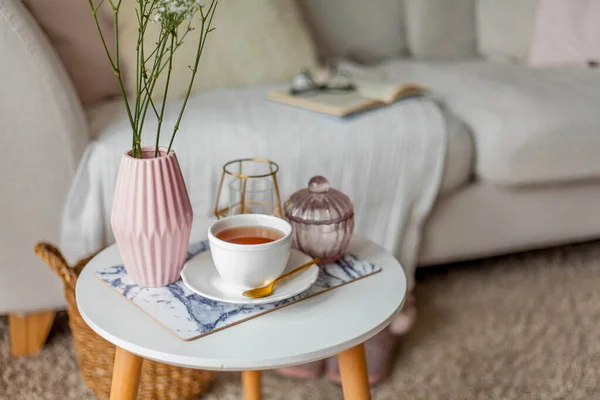 Spring home cozy interior. A bouquet of flowers in a vase, a cup of tea, decor on a coffee table. Mood.