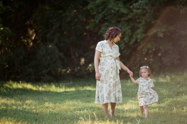 Genç ve güzel bir anne ve küçük kızı tarlada çiçek topluyor. Annelik. Bir aile. Yaz.