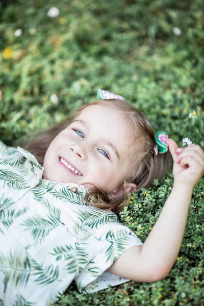 La niña linda está sentada en la hierba. Chica feliz en el parque. Verano . —  Fotos de Stock