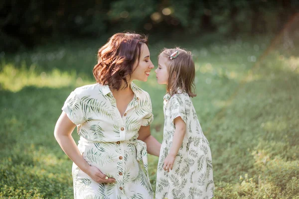 A beautiful young pregnant mom and her little daughter are picking flowers in a field. Motherhood. A family. — Stock Photo, Image
