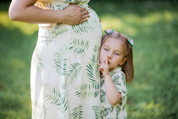 A beautiful young pregnant mom and her little daughter are picking flowers in a field. Motherhood. A family. Summer.