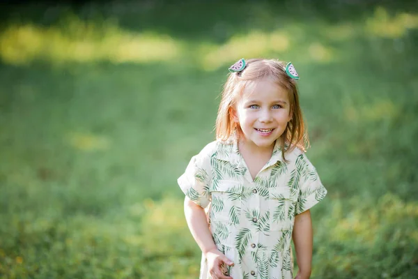 La niña linda está sentada en la hierba. Chica feliz en el parque. Verano . — Foto de Stock