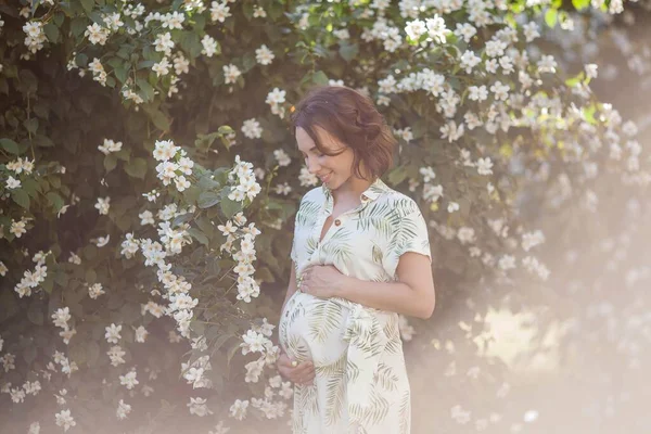 Bela jovem mulher grávida feliz está de pé perto da árvore florescente. Maternidade. Com amor. Primavera . — Fotografia de Stock