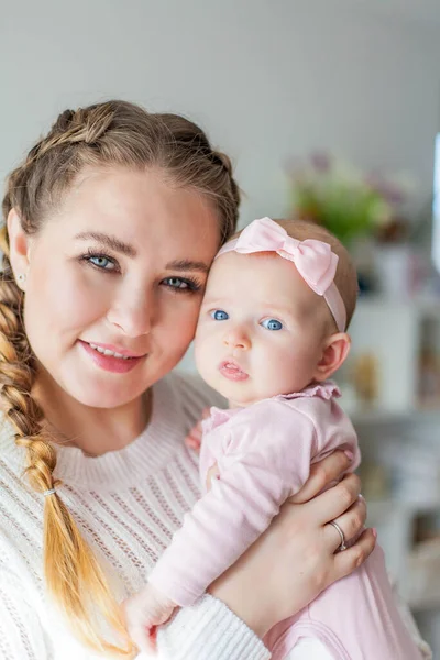 Una bella giovane madre tiene tra le braccia una piccola figlia di 2 mesi dagli occhi azzurri. Neonato . — Foto Stock