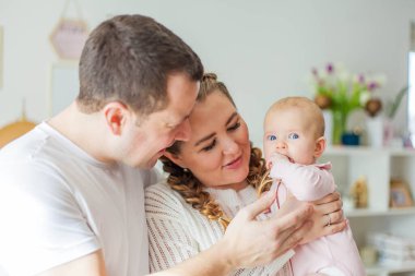 Güzel, genç ebeveynler yeni doğmuş kızlarını kollarında tutuyorlar. 2 aylık mavi gözlü küçük kız..