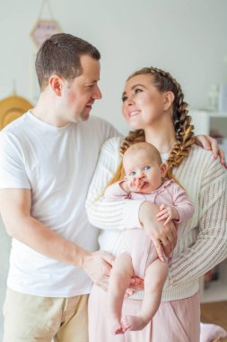 Güzel, genç ebeveynler yeni doğmuş kızlarını kollarında tutuyorlar. 2 aylık mavi gözlü küçük kız..