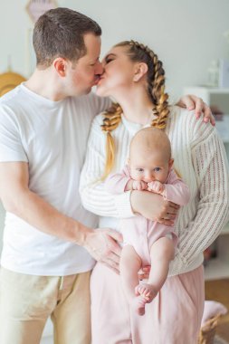 Güzel, genç ebeveynler yeni doğmuş kızlarını kollarında tutuyorlar. 2 aylık mavi gözlü küçük kız..