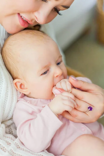 Close-up. A beautiful young mother holds in her arms a small pretty blue-eyed 2-month-old daughter. Newborn. — Stock Photo, Image