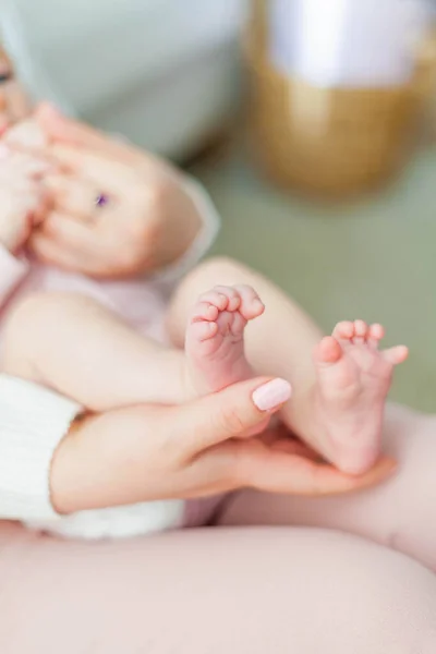 Close-up. Beautiful young mother holds in her hands the legs of her little daughter. Baby. Newborn. — Stock Photo, Image