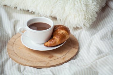 Bir fincan sıcak kakao, kruvasan, yatakta ahşap bir tezgah. Karantina zamanı. Homellik. Samimi.