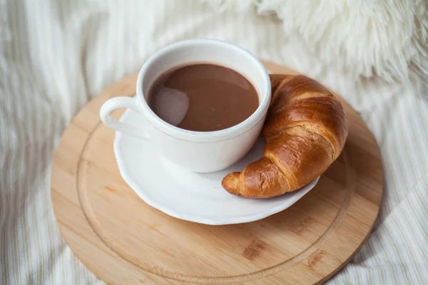 A cup of hot cocoa, a croissant, a wooden stand on the bed. Quarantine time. Homeliness. Cozy.