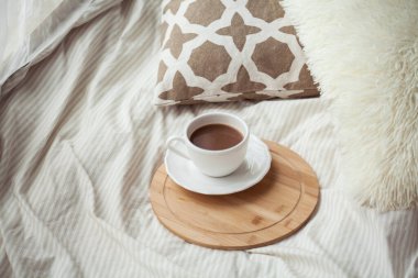 Bir fincan sıcak kakao, yatağın üzerinde ahşap bir stant. Karantina zamanı. Homellik.