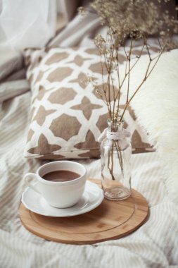 Bir fincan sıcak kakao, ahşap bir tezgah, yatağın üzerindeki cam vazoda kurumuş bir çiçek. Homellik.