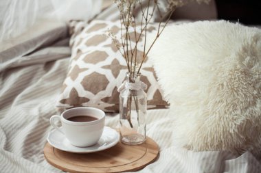 Bir fincan sıcak kakao, ahşap bir tezgah, yatağın üzerindeki cam vazoda kurumuş bir çiçek. Homellik.