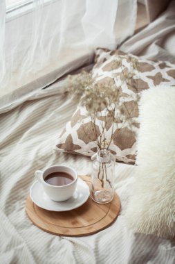 Bir fincan sıcak kakao, ahşap bir tezgah, yatağın üzerindeki cam vazoda kurumuş bir çiçek. Homellik.