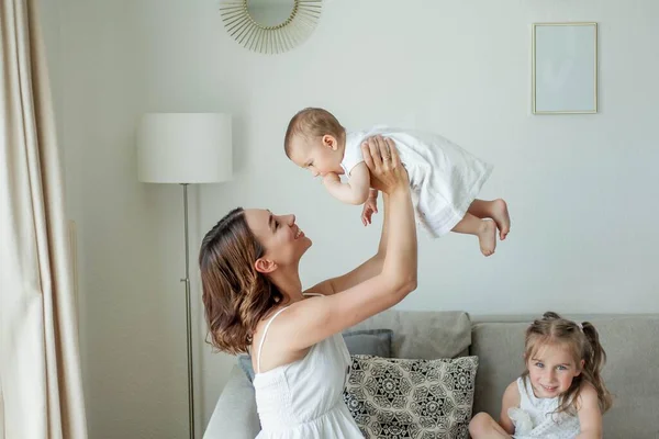 어린 어머니는 집안에서 딸들 과 함께 행복 한 모습을 하고 있습니다. 어머니들의 날. — 스톡 사진