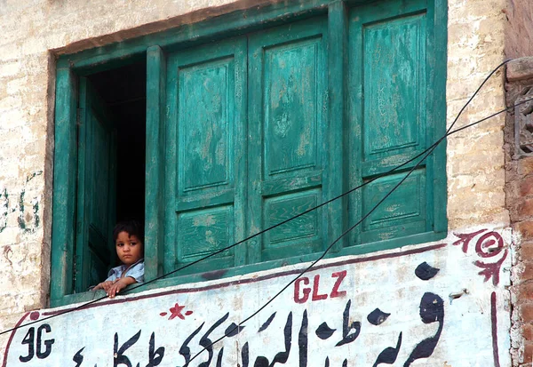 パキスタンのKhyber Pakhtunkhwa州でのペシャワール 若いパキスタン人の少年がペシャワールの窓から外を見ていた 小さな男の子が窓の外を見ている 緑の木製のシャッター パキスタンのペシャワール — ストック写真