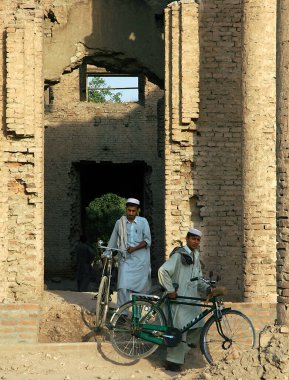 Afganistan, Nangarhar Eyaleti 'ndeki Jalalalabad. Afganistan, Celalabad 'daki Seraj-ul Emorat harabelerinin önünde bisikletli iki adam. Afgan erkekler, bisikletler, Celalabad, Afganistan.