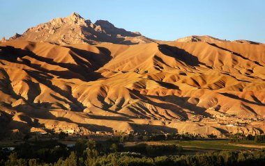 Orta Afganistan 'da Bamyan (Bamiyan). Bamyan (Bamiyan) Vadisi 'nin üzerinde alçak güneş tarafından aydınlatılmış gölgeli altın dağları gösteren bir manzara. Kasaba Afganistan 'ın ünlü UNESCO Buda' larına ev sahipliği yapar..