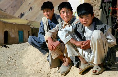 Bamyan (Bamiyan) ilindeki Syadara (Siyah Darah), Afganistan. Orta Afganistan 'ın küçük bir kasabası olan Syadara' da yol kenarında oturan ve çömelmiş üç genç Afgan.. 
