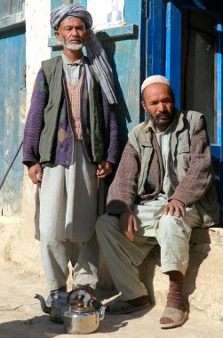 Bamyan (Bamiyan) ilindeki Syadara (Siyah Darah), Afganistan. Afganistan 'ın orta kesimindeki Syadara kasabasının girişinde Afgan erkekler. Türbanlı, kafatası şapkalı ve çaydanlıklı adamlar..