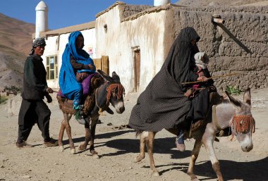 Bamyan (Bamiyan) ilindeki Syadara (Siyah Darah), Afganistan. Afgan adam Orta Afganistan 'ın Syadara kasabasında eşeklere binen iki kadının arkasında yürüyor. Kadınlı ve eşekli bir adam