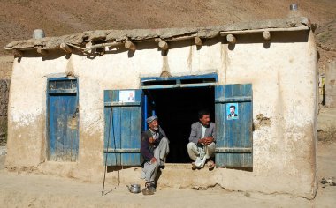 Bamyan (Bamiyan) ilindeki Syadara (Siyah Darah), Afganistan. Orta Afganistan 'ın küçük Syadara kasabasında bir evin girişinde iki Afgan adam oturuyor. Sarıklı ve çaydanlıklı bir adam.