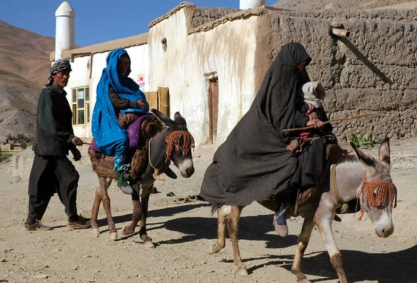stock image Syadara (Siyah Darah) in Bamyan (Bamiyan) Province, Afghanistan. Afghan man walks behind two women riding donkeys in the town of Syadara in Central Afghanistan. Man with women and donkeys