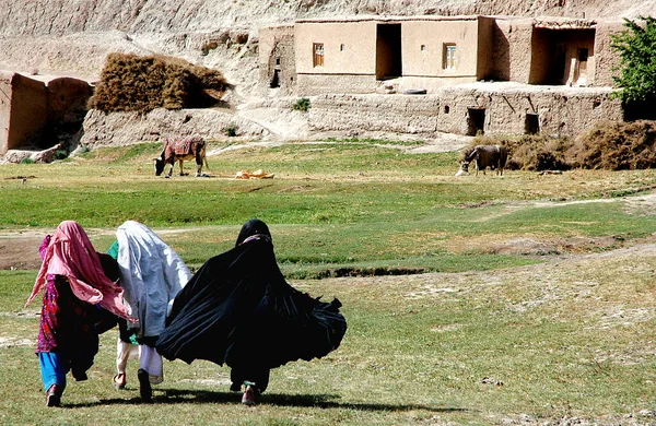 Afganistan 'ın Ghor Eyaleti' ndeki Chaghcharan ve Jam Minaresi arasında küçük bir köy. Yerel kıyafetli üç genç kadın Orta Afganistan 'ın ücra bir köşesindeki evlerine doğru koşuyor..