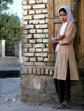 Faryab Eyaleti, Afganistan 'da Maymana. Maymana 'da sokakta duran bir kız bisküvi yiyor ve başörtüsü takıyor. Maymana batı Afganistan 'da..