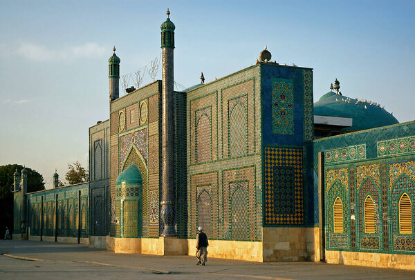 Мазари-Шариф, провинция Балх в Афганистане. Мужчина проходит мимо Голубой мечети в Мазар и Шариф на солнце. Красочные мозаики и плитки украшают стены мечети. Северная Афганистан
.